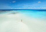 Fototapeta Na sufit - Aerial view of alone young woman on the sandbank in ocean, white sand, blue sea during low tide at sunny summer day in Nakupenda, Zanzibar island. Top view of girl, sand spit, water, sky with clouds