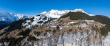 Fototapeta Miasto - Aerial view of Murren, Switzerland, showcases a serene mountain village with traditional chalet style buildings on a cliff. Snow covered Swiss Alps and clear skies create a picturesque backdrop.