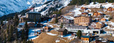 Fototapeta Miasto - Aerial view of Murren, Switzerland, showcases a serene mountain village with traditional chalet style buildings on a cliff. Snow covered Swiss Alps and clear skies create a picturesque backdrop.