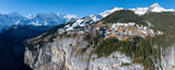 Fototapeta Miasta - Aerial view of Murren, Switzerland, showcases a serene mountain village with traditional chalet style buildings on a cliff. Snow covered Swiss Alps and clear skies create a picturesque backdrop.