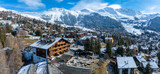Fototapeta Miasta - Aerial panoramic view of the Verbier ski resort town in Switzerland. Classic wooden chalet houses standing in front of the mountains. 