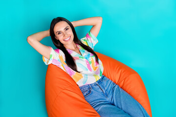 Poster - Photo of adorable woman wear trendy print clothes hold arms behind head comfy furniture isolated on cyan color background