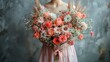   A woman wearing a pink dress cradles a bouquet of pink and white blossoms against a gray backdrop with a blue background