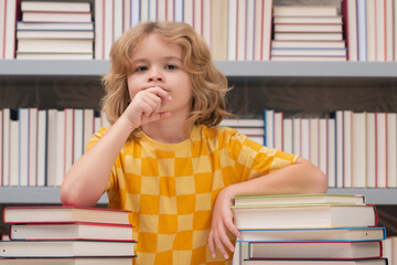 Poster - Elementary schoolboy. School boy doing homework on desk in school library. Pupil child studying homework literature near pile of books. Kid reads a book with shelves stacks of books.