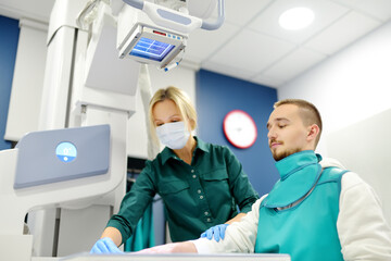 Wall Mural - Female radiologist going to made x-ray shot of young man hand in x-ray room in modern clinic. Patient wearing in protect lead apron