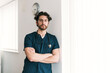 © ADDICTIVE STOCK - A pensive male healthcare worker with arms crossed stands by a clock, symbolizing timely medical services