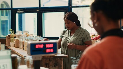 Canvas Print - Customer checking organic bio merchandise in grocery store, looking for additives free pasta or pantry items to buy weekly supplies. African american woman searching for nonpolluting goods.