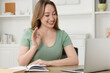 © New Africa - Young woman waving hello during video chat via laptop at wooden table indoors