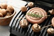 Electric grill with homemade sausage, rosemary and mushrooms on rustic wooden table, closeup