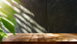 Empty wooden table next to a black wall, dark tones, with plant leaves and shadows outdoors. Brown table with copy space for product advertising mockup. Terrace, balcony, backyard on a sunny day.