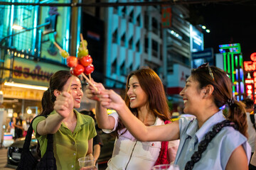 Wall Mural - Asian women friend eating street food while traveling in city at night. 