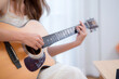 Closeup hands of young asian woman sitting on sofa playing guitar in living room at home, skill and practice, guitarist and hobby with enjoyment and relax, entertainment and lifestyle.