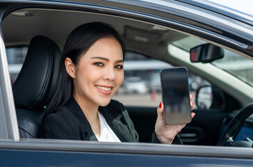 Wall Mural - Young beautiful asian business women getting new car using smartphone. she very happy and excited. she showing cell phone screen application. Smiling female driving vehicle on the road downtown city