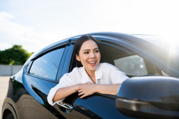 Wall Mural - Young beautiful asian business women getting new car. Happy smiling female driving vehicle on the road Sticking her head outta the windshield with sun light. Business woman buying driving new car