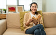 © Chanakon - Asian beautiful woman sitting reading book on cozey couch sofa in living room with sun light morning. People female stay home part time relax at home.