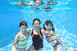 Family swims underwater in swimming pool, happy active mother and children have fun under water, fitness and sport with kids on summer holiday vacation