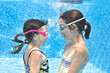 Kids swim in swimming pool underwater, little active girls have fun under water, children fitness and sport on family vacation
