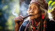 Close-up of an older Asian woman of the Akha tribe, wearing traditional clothes, necklaces. jewelry smoking a pipe with smoke in Myanmar.