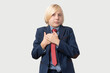 © somemeans - Portrait of young businesswoman with blond hair, dressed in blue suit and red tie, keeps hands on chest, looks seriously at camera, isolated over white background