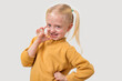 Portrait of a cute little girl in a yellow sweater showing ok sign with fingers