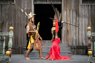 Portrait of man and woman wearing traditional Kalimantan Dayak clothing with the background of a traditional Dayat house called 