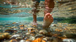 Close-up of a boy's feet kicking in the clear water of a stream, with pebbles and small fish visible beneath the surface.