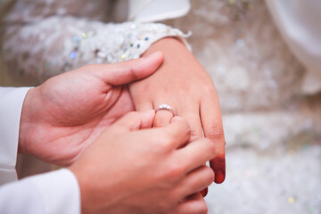 Wall Mural - Groom put a ring on finger of his lovely wife. Close up image and selective focus.