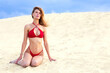 Beautiful young woman in red bikini sitting on sand dune.