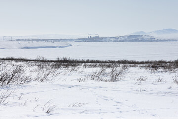 Wall Mural - Arctic landscape. View of the snow-covered tundra and the frozen wide river. In the distance is the city of Anadyr, Chukotka Autonomous Okrug, Far North of Russia. Cold winter weather.