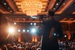 Over-the-shoulder view of a well-dressed businessman giving a speech at a corporate seminar in a hotel ballroom.