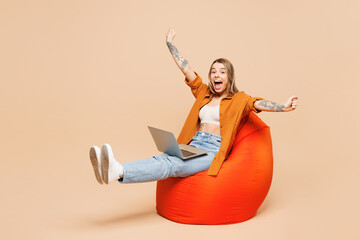 Wall Mural - Full body young IT woman she wear orange shirt casual clothes hold use work on laptop pc computer do winner gesture isolated on plain pastel light beige background studio portrait. Lifestyle concept.