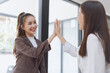 © SOMKID - Businesswoman partnership handshake concept. Two young asian business professionals celebrating teamwork in an office, Colleague in meeting.