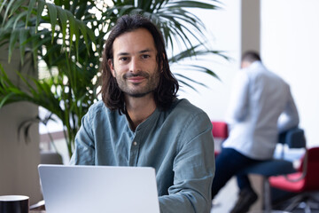 Poster - portrait d'un employé de bureau, homme d'affaires sympathique assis qui travaille avec un ordinateur portable. Il regarde la caméra en souriant