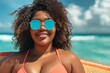 Plus size African American woman wears peach swimwear and standing with surfboard on the sunny beach