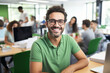 © Ivan - A cheerful man in glasses and a green T-shirt smiles at the camera. Happy office worker at desk with computer or laptop with team blured in background