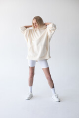 Wall Mural - Beautiful blonde woman posing in white hoodie and leggings posing against white background