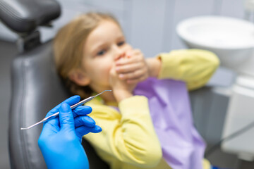 So scared. Little girl sitting in dentist chair and covering her mouth, being afraid of the checkup at the dentists office