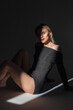 © alones - Beautiful fresh sensual girl model in a fashion black dress sits on the floor in the studio in the dark with light