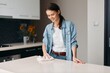 © SHOTPRIME STUDIO - Cleaning the Modern Kitchen: One Happy Housewife Wiping the Table with Detergent Spray, wearing Casual Attire
