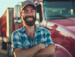 Zoung male truck driver standing in front of his truck, arms crossed, smiling at the camera, bearded man, wearing a hat 