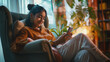 A cheerful millennial Indian girl unwinds at home, resting in an armchair while typing on her smartphone and using an online app, Concept for relaxation