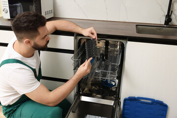 Poster - Serviceman examining dishwasher cutlery rack in kitchen