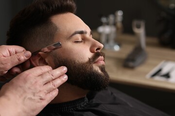 Poster - Professional barber shaving client's beard with blade in barbershop, closeup