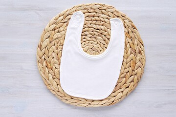 Wall Mural - White cotton baby bib mockup for design presentation, baby announcement, flat lay on wicker mat.