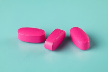 Closeup shot of three magenta caplets on the cyan background