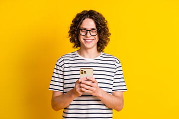 Poster - Photo portrait of handsome teenager guy hold device chatting friend dressed stylish striped garment isolated on yellow color background