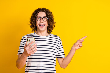 Poster - Photo portrait of handsome teenager guy hold device point empty space dressed stylish striped garment isolated on yellow color background