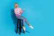 Full length photo of pretty girl wear checkered pullover sit on chair indicating at discount empty space isolated on blue color background