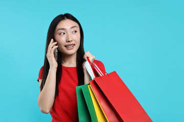 Poster - Smiling woman with shopping bags talking by smartphone on light blue background. Space for text