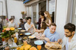 © Maskot - Group of male and female multiracial friends having food and drinks at dinner party in balcony